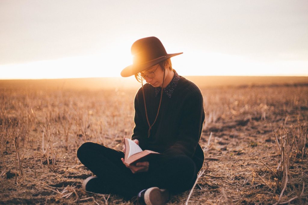 young man sits on the ground reading book