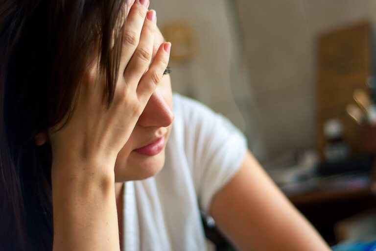 young hungover woman sitting with head in her hands wondering what is binge drinking